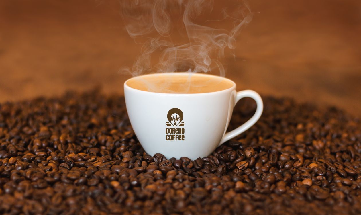 A white ceramic Coffee mug with the 'DORERO COFFEE' logo, featuring a stylized face, sitting on  a bed of roasted coffee beans, with steam rising from the hot coffee inside the mug